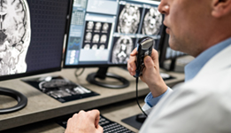 Cropped view of radiologist viewing MRI scan results and dictating report. Focused on hand holding voice recorder. Examination at specialized medical clinic, diagnosis and healthcare concept.